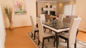 Un coin repas avec une table en verre, six chaises, un vase de fleurs et un tableau au mur.