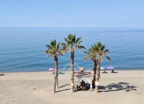 A beach with palm trees, a covered seating area, and umbrellas. - Quiet Beachfront Apartment (La Herradura)