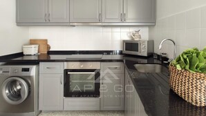 Una cucina moderna con mobili grigi, forno a incasso, microonde, lavatrice e lavello.