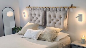 Una camera da letto con testiera capitonata, due comodini con lampade e uno specchio a parete.