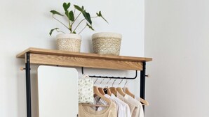 Un portabiti in legno con uno specchio, su cui sono appesi diversi capi d'abbigliamento e un cesto di vimini.