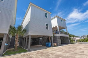 A modern residential building with a covered parking area, a small palm tree, and a clear blue sky.