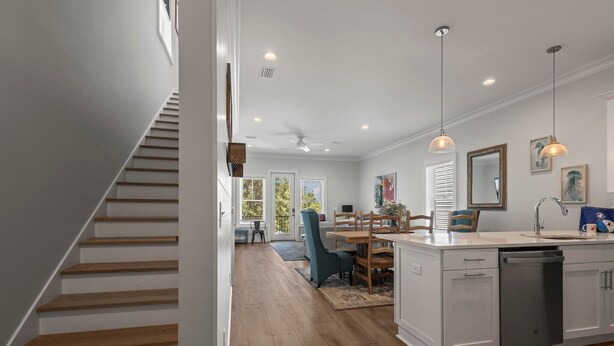 A modern kitchen with a central island, wooden staircase, and a dining area with a blue chair. - Sea At Last- Family Fun, Close To Community Pool! (Gulf Shores)