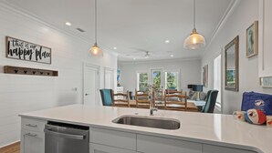 A modern kitchen with a central island, pendant lights, and a view into the dining area. - Sea At Last- Family Fun, Close To Community Pool! (Gulf Shores)