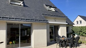 Una casa con un patio, un portón corredizo de vidrio y una pequeña mesa exterior con sillas.