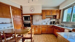 Una cocina con armarios de madera, una mesa de comedor con sillas, un microondas, un horno y una ventana con vistas a árboles.