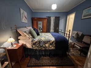 A bedroom with a bed, nightstand, lamp, chair, and a mirror.