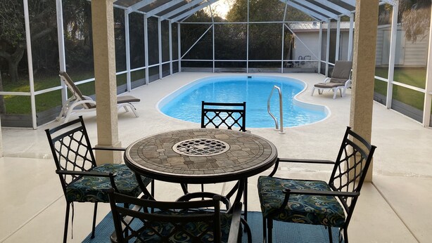 Ein überdachter Außenbereich mit Pool, Tisch und Stühlen sowie Blick auf den Garten.