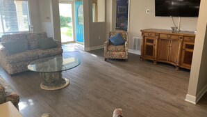 Ein Wohnzimmer mit einer Couch, einem Sessel, einem Glastisch, einem Holzschrank und einem Flachbildfernseher.