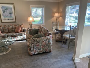 A living room with a floral-patterned sofa, a glass coffee table, and a dining table with chairs.