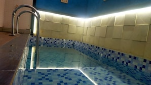 A swimming pool with blue and white checkered tiles, a metal handrail, and a wall with a blue and beige pattern. - Azzima villa  (Batu)