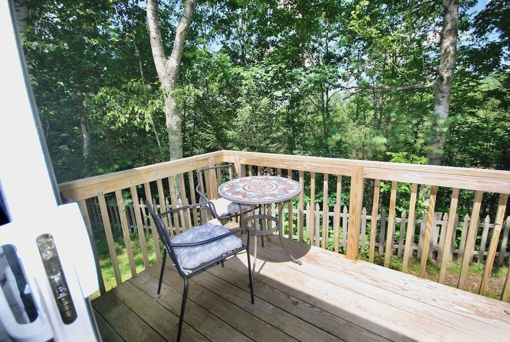 A wooden deck with a table and chairs, surrounded by a wooden fence and trees.