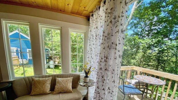 Ein gemütliches Wohnzimmer mit einer Couch, einem kleinen Tisch und Blick auf einen Garten durch große Fenster.