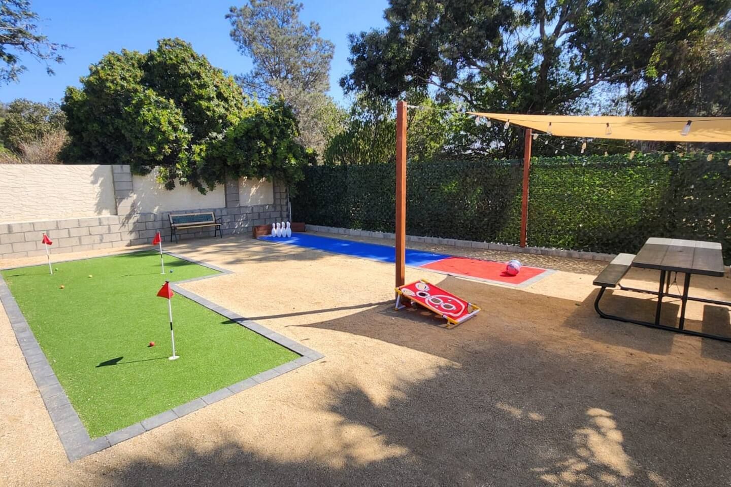 A backyard with a putting green, sand trap, and a picnic table.