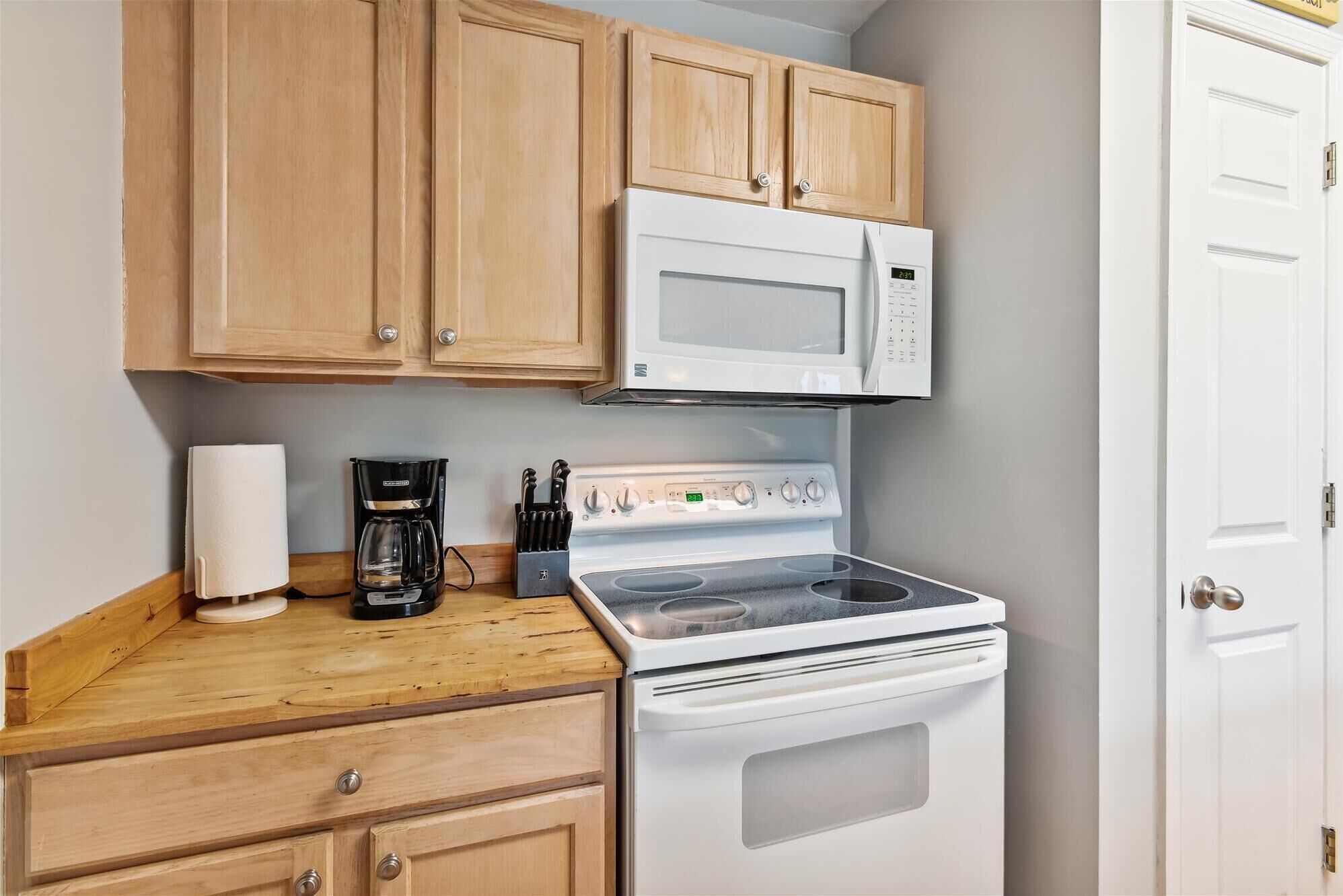 A kitchen with wooden cabinets, a white microwave, a stove, and a coffee maker.