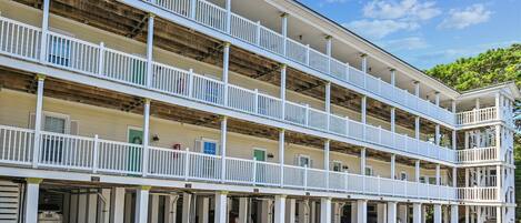 A multi-story building with balconies and a covered parking area.