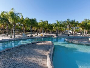 Uma área de piscina com caminhos de azulejo e palmeiras.