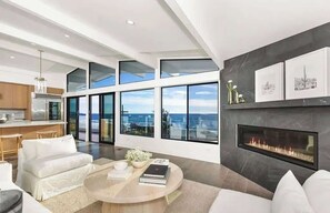 A modern living room with a fireplace, large windows, and a view of the ocean.