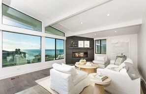 Un salon moderne doté de grandes fenêtres, d’une cheminée et de meubles blancs.