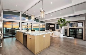 Une cuisine moderne dotée d’un grand îlot central, de luminaires suspendus et de grandes fenêtres offrant une vue dégagée.