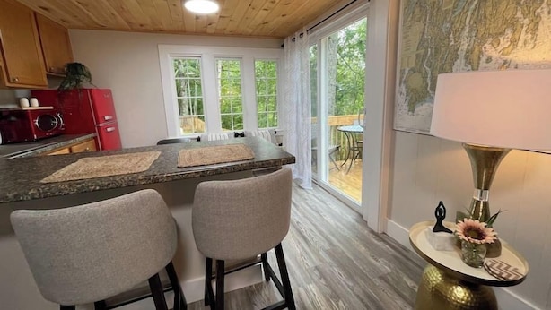 A kitchen with wooden ceiling, a bar area with two chairs, a red appliance, and a view of the outdoors. - Spacious 1 Bedroom Close to Everything 4 (Edgecomb)