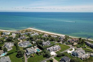Vue aérienne d’une zone résidentielle côtière, avec des maisons, une plage et un océan bleu limpide.