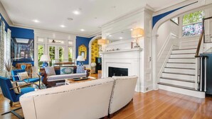 A spacious living room with a white sofa, a fireplace, and a staircase leading to an upper level. - Luxurious Estate, Private Heated pool! (West Harwich)