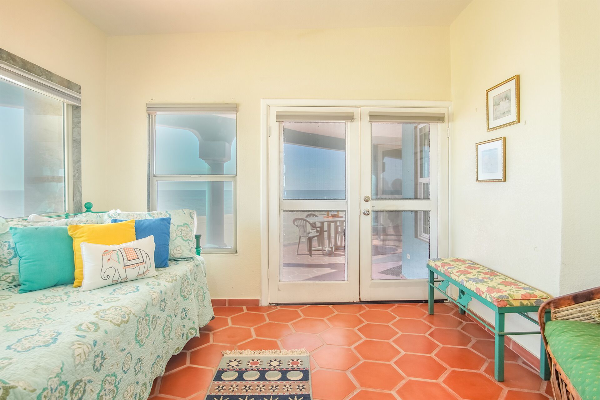 A room with a patterned sofa, a bench, and a door leading to an outdoor area with a table and chairs.