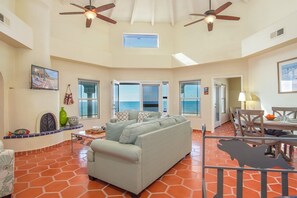 Relax in this spacious living area with a sofa facing the sea view, a dining table for two, and a high ceiling with ceiling fans.