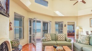 Amplia sala de estar con un sofá verde, una mesa de centro con adornos y vistas a la playa a través de grandes ventanales.