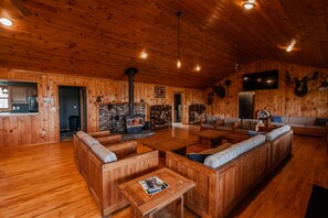 Interior de una cabaña de madera con chimenea, zona de estar y cocina con armarios de madera.