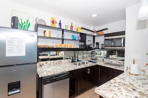 A modern kitchen with a stainless steel refrigerator, a dishwasher, a double sink, and a microwave.
