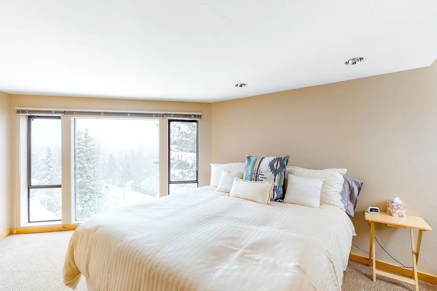 Quarto com uma cama grande, duas janelas e uma mesinha de cabeceira com abajur.