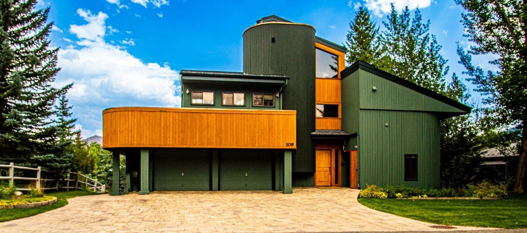 Uma casa moderna de dois andares com fachada verde, porta de garagem de madeira e céu azul límpido.