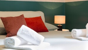 Una cama bien tendida con dos almohadas, una lámpara de noche y toallas enrolladas.