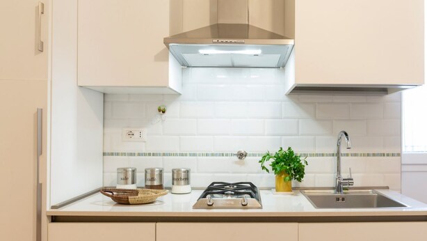 Una cocina con estufa a gas, pileta de acero inoxidable y campana extractora moderna.