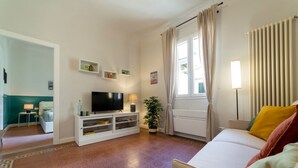 Una sala de estar con televisor, sofá y ventana con cortinas.