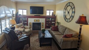 Una sala de estar con chimenea, televisor, un reloj y una estantería.