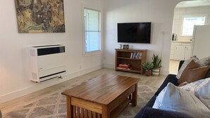 Ett vardagsrum med ett soffbord i trä, en mörkblå soffa, en platt-TV, en bokhylla och en stor, abstrakt tavla på väggen.