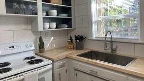 Ett modernt kök med vita skåp, en inbyggd ugn, en diskho och ett fönster med persienner.