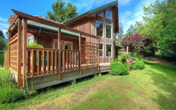 Surrounded by lush greenery, this cabin-style building features a spacious deck with a pergola and wooden railing.