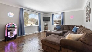 A living room with a brown sofa, a jukebox, and a TV on the wall. - Rock n Roll! DT 2bd home! Walk to beach, bars&more (Port Sanilac)