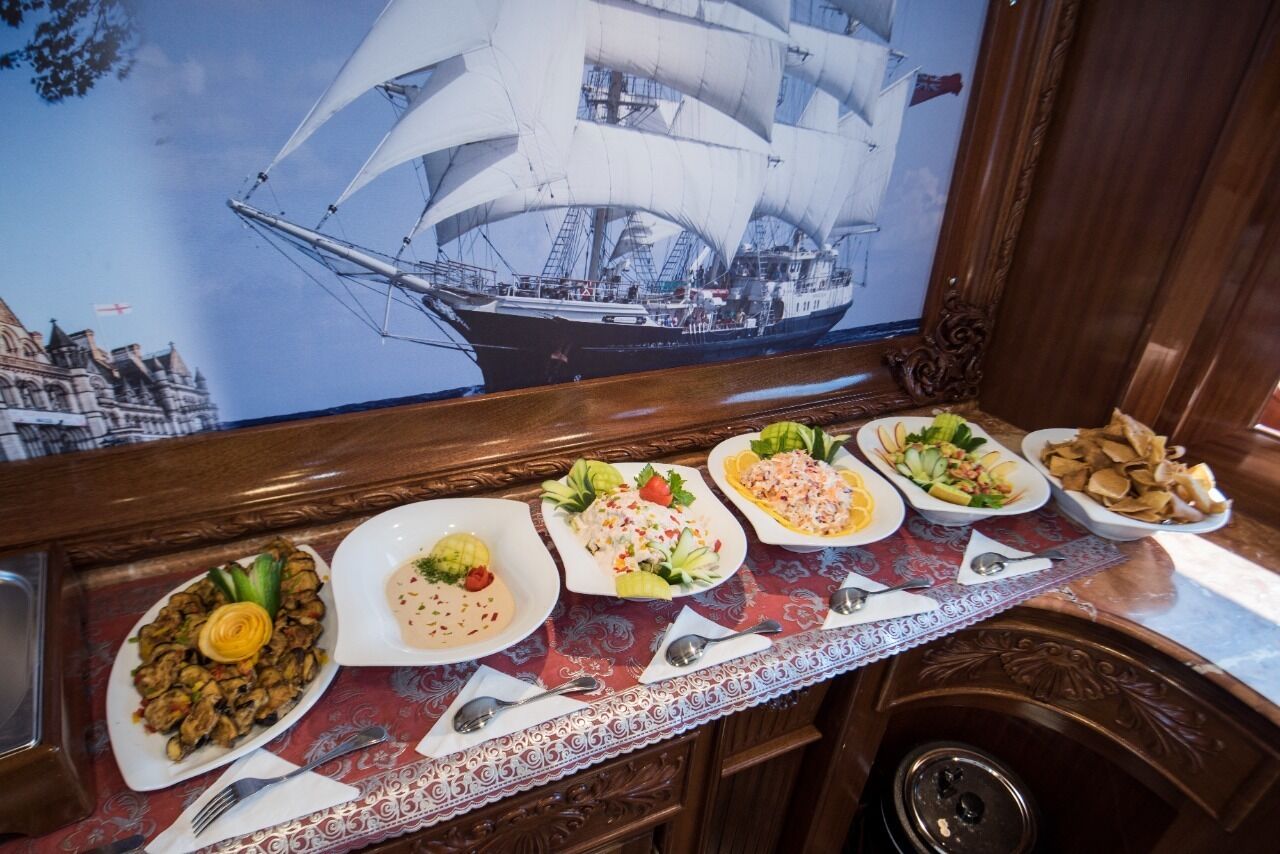A dining table with various dishes, a ship painting, and a wooden cabinet.