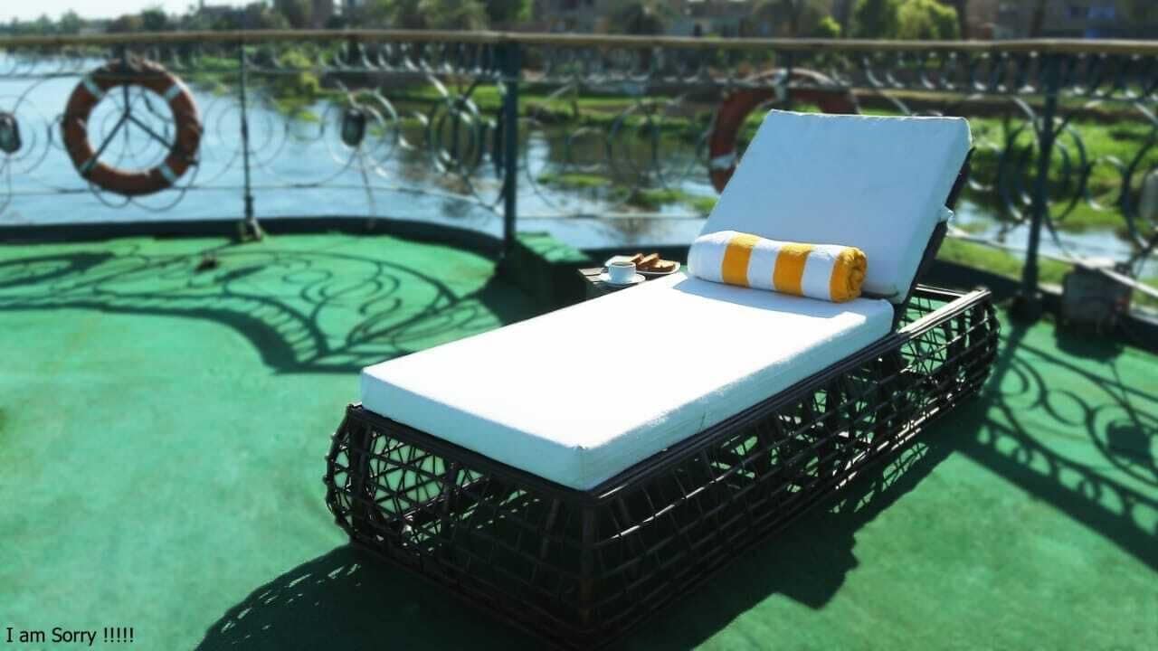 Un lit simple avec un matelas blanc et un oreiller à rayures jaunes et blanches, sur un balcon dont le sol est vert.