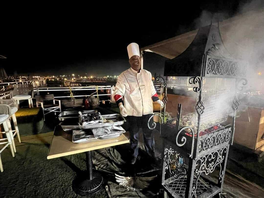 Un cocinero en un puesto de comida con una parrilla, equipo de cocina y una mesa con bandejas y utensilios.