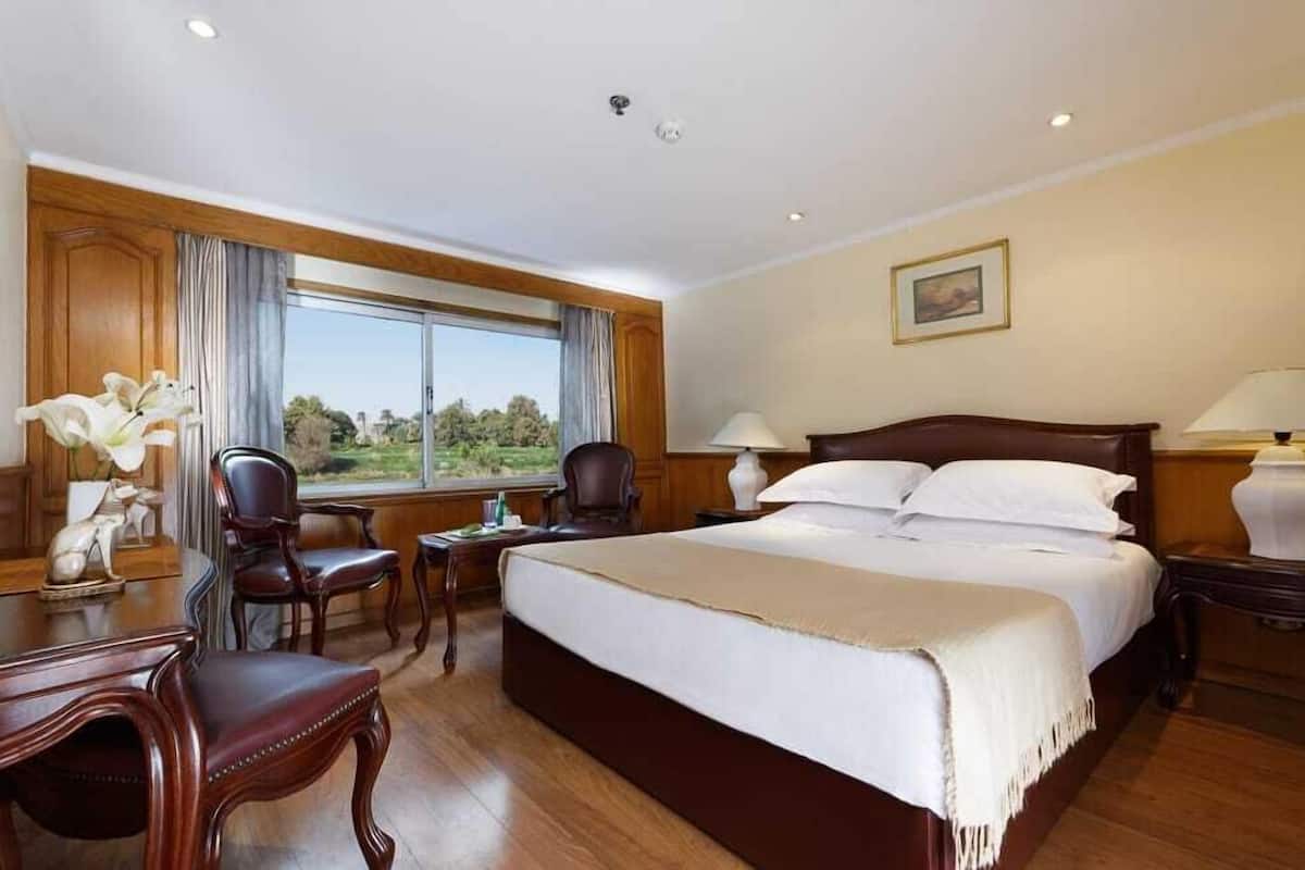Amplia habitación de hotel con una cama grande, muebles de madera, una mesa de comedor y vistas al exterior.