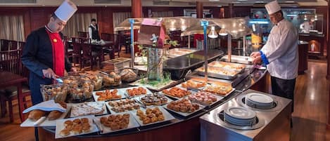 Una mesa de buffet con diversos alimentos y dos chefs preparándolos.