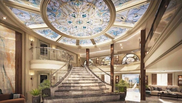 Un vestíbulo imponente con una escalera de mármol, un techo alto con detalles ornamentales y vistas a una amplia sala de estar.