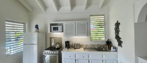 A compact kitchen with white cabinetry, a gas stove, a microwave, and a refrigerator.