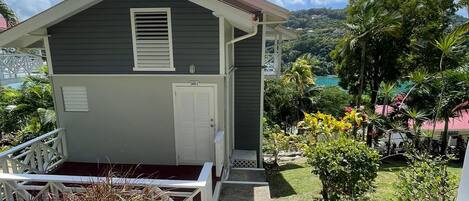 A two-story house with a front porch, a staircase leading to the entrance, and a view of a lush garden and mountains in the background.